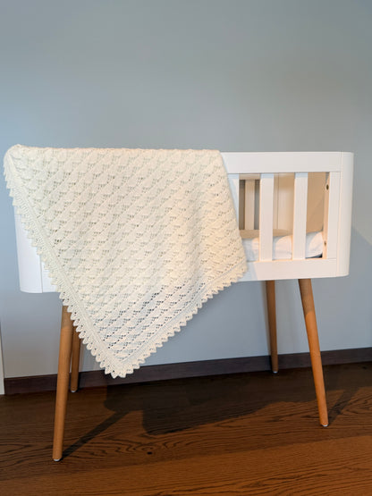 Hvitt strikket babyteppe med strukturmønster over en hvit barneseng