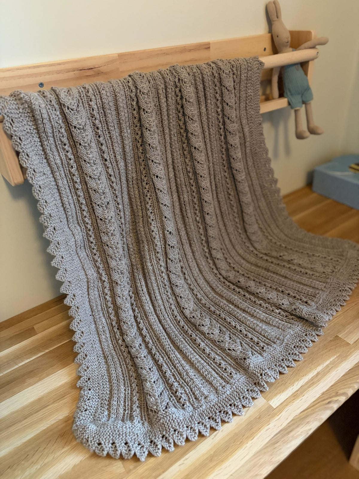 Lys beige Ingrid-babyteppe henger over et trestativ ved siden av en kosekanin.